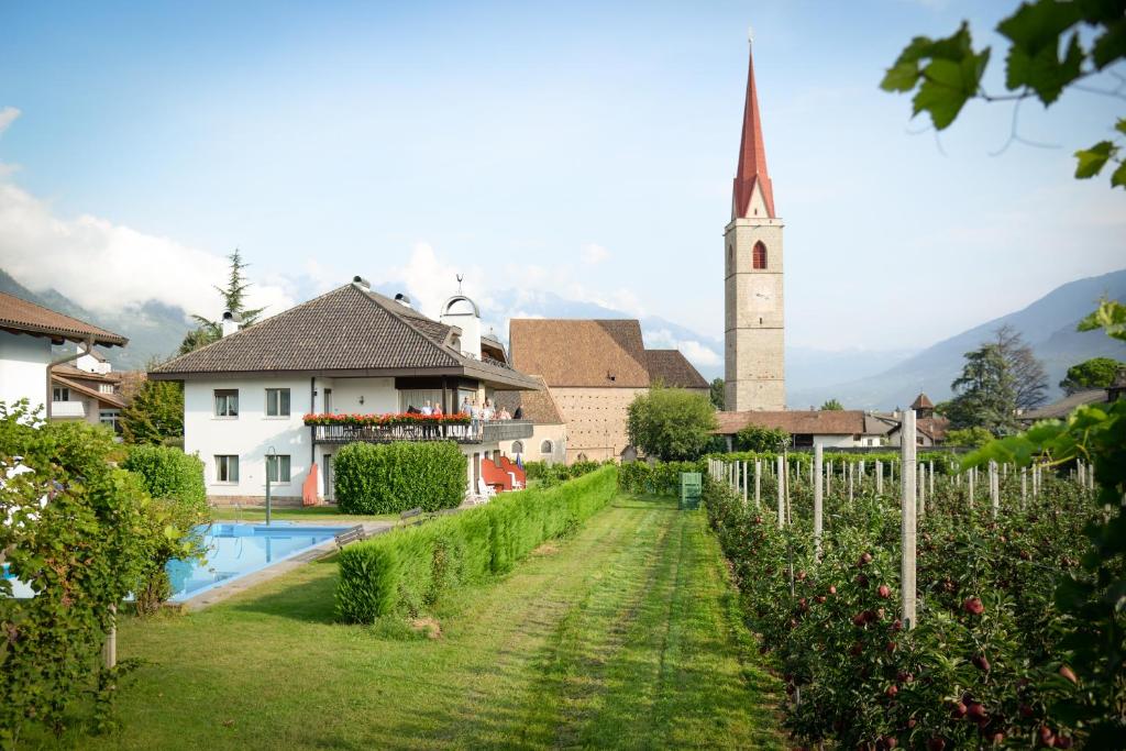a village with a church and a yard with a pool at Pension Rebgut in Lana