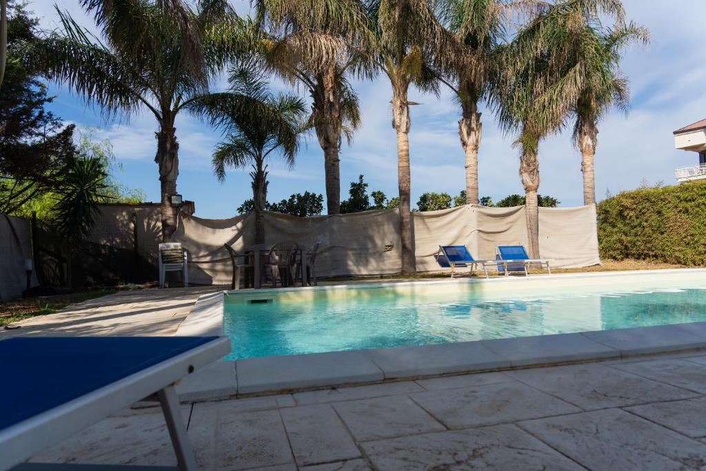 una piscina con palmeras en el fondo en Petite Maison en Marzamemi