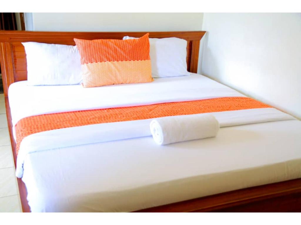 Macchiato Suites في كيغالي: سرير أبيض عليه وسائد برتقالية وبيضاء
