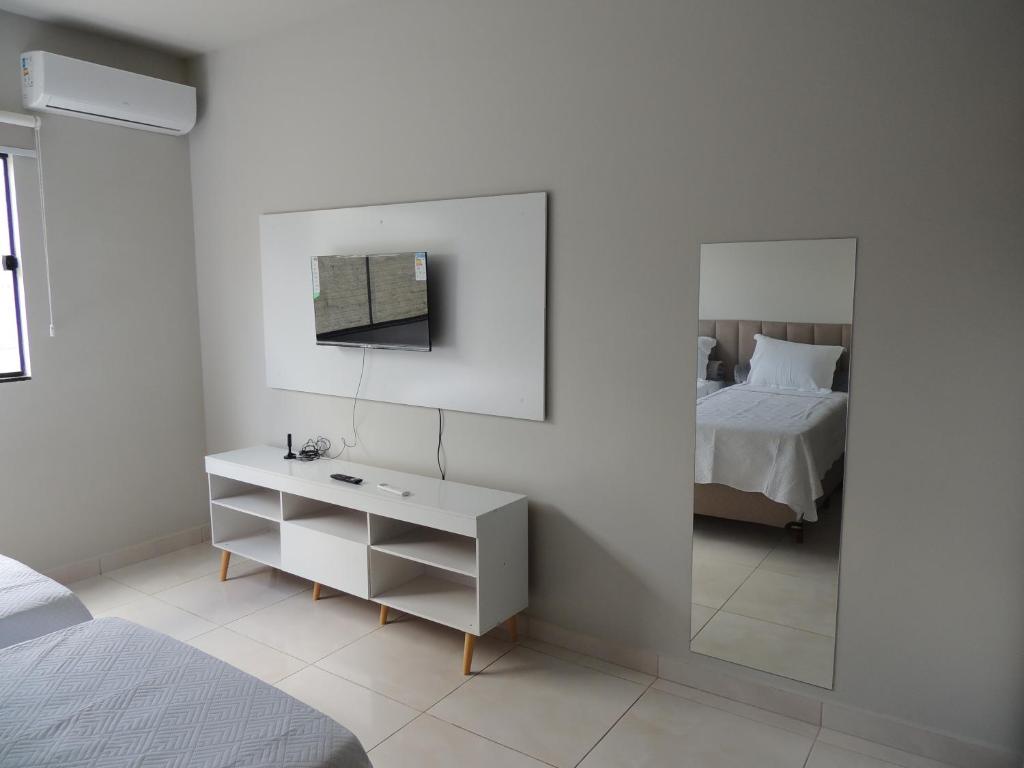 a white bedroom with a bed and a mirror at Porto Residence in Vitória da Conquista