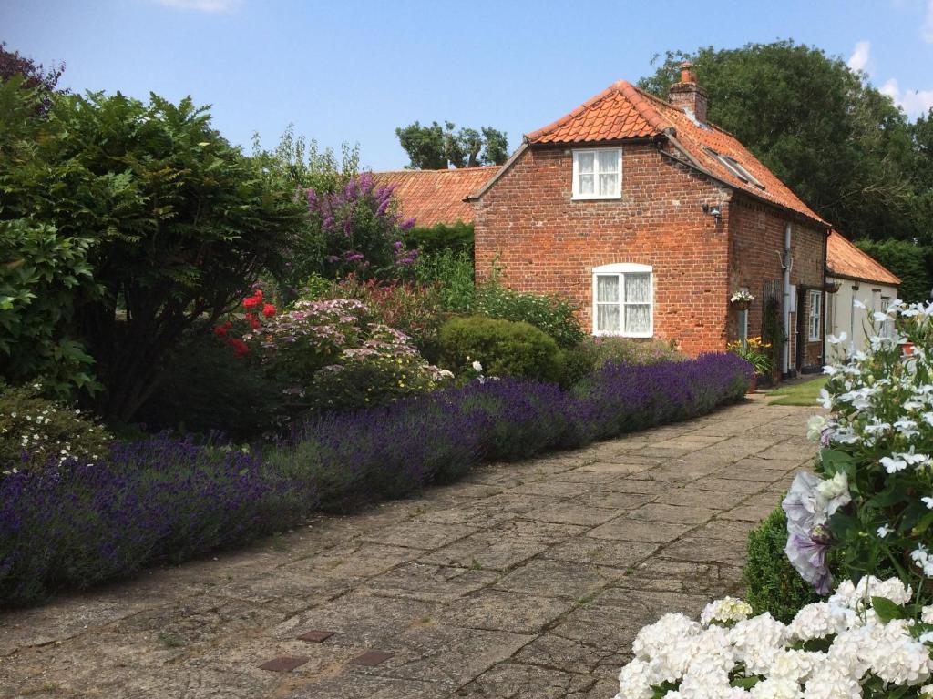 a brick house with a garden of flowers at Dolls House Cottage in Hilborough