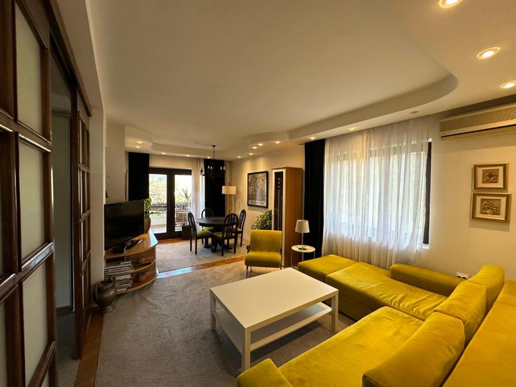 uma sala de estar com um sofá amarelo e uma televisão em OKSA APARTMENT em Skopje
