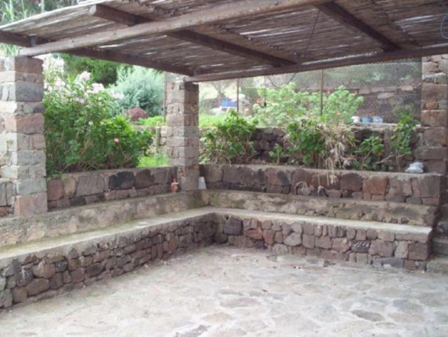 a stone retaining wall with a bench under a pergola at il patio mini appartamento in Pantelleria
