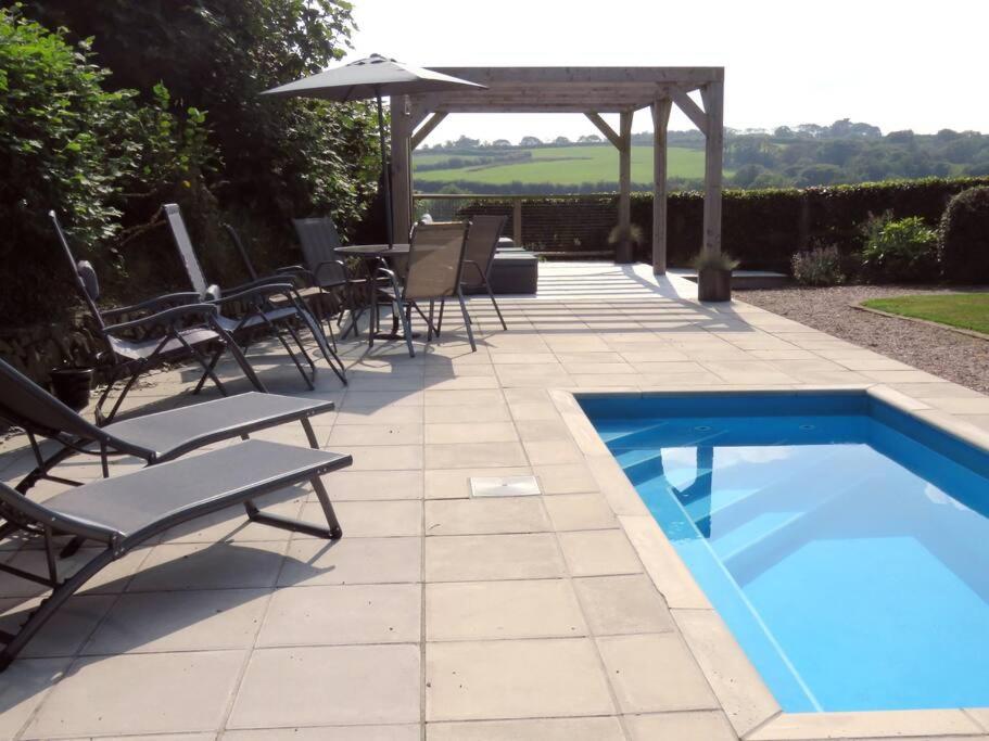 a swimming pool with chairs and a table and an umbrella at Ochre Cottage in Holsworthy