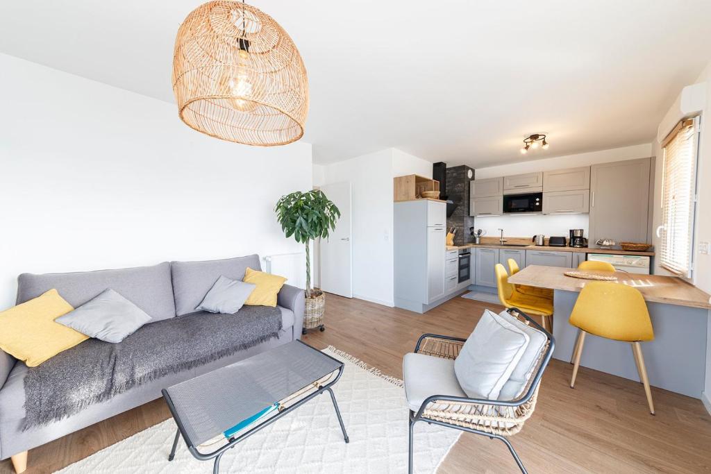 a living room with a gray couch and a kitchen at Le Magellan - logement neuf, parking, grand balcon in Dinard
