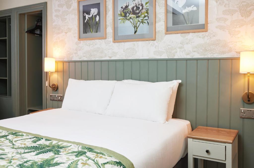 um quarto com uma cama branca e quadros na parede em The Kings Head Wroxham by Greene King Inns em Wroxham