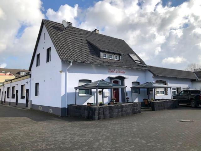 ein weißes Gebäude mit Sonnenschirmen auf einem Parkplatz in der Unterkunft Motel de Winter - Motel - Apartmenthaus - Monteurzimmer in Castrop-Rauxel