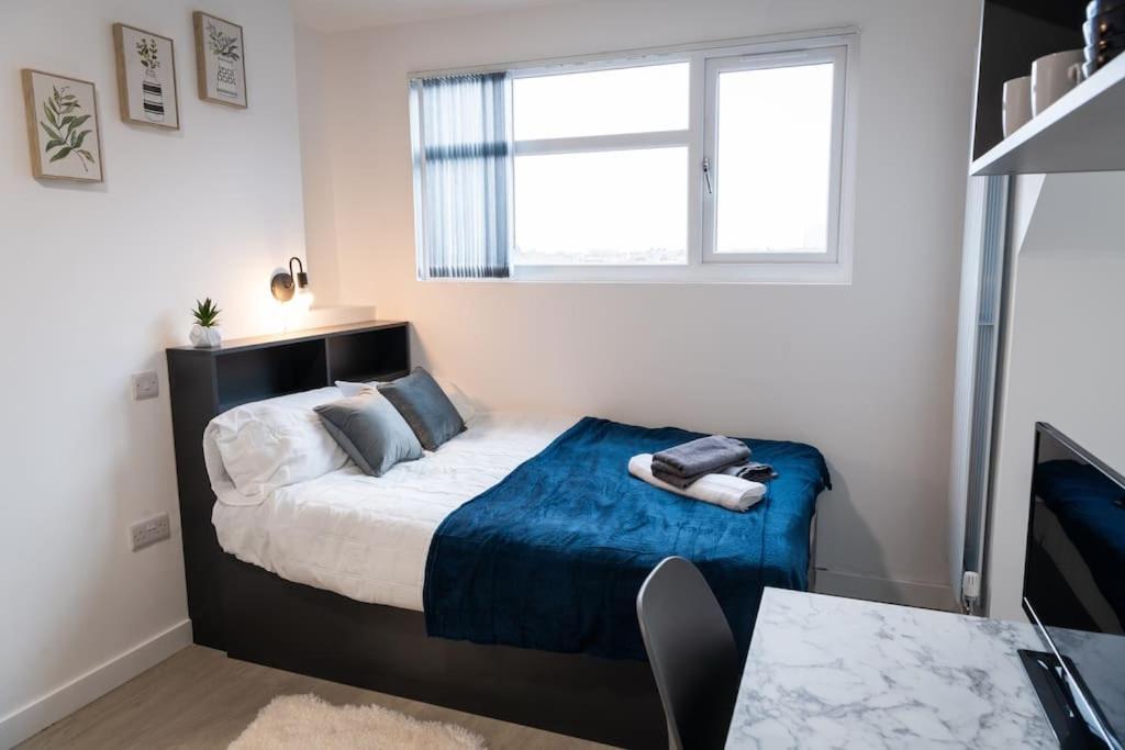 um quarto com uma cama com um cobertor azul e uma janela em Old Trafford : Stunning Studio em Manchester