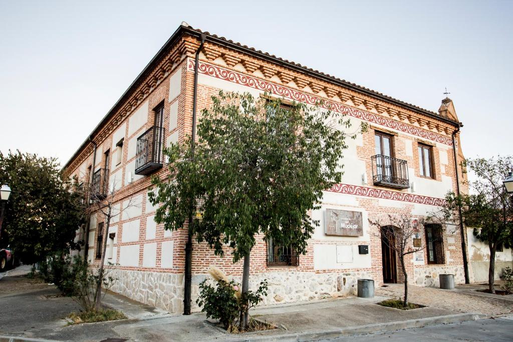 un vieux bâtiment en briques avec un arbre devant lui dans l'établissement Posada Real by Alterhome, à Velayos