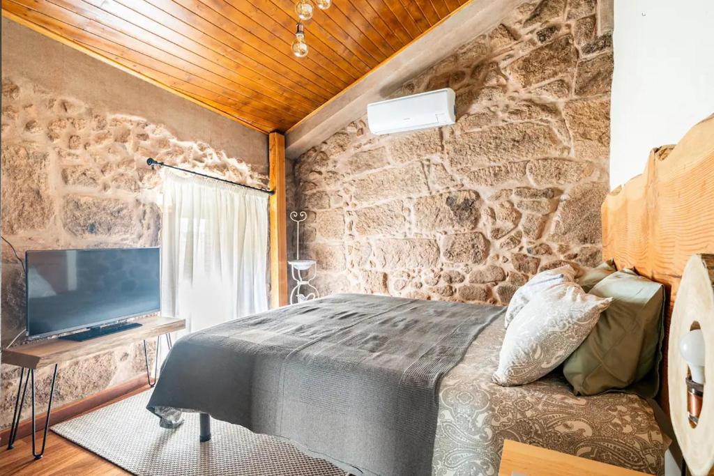una camera da letto con un muro in pietra, un letto e una TV di Segredos da Montanha - Mangualde a Mangualde