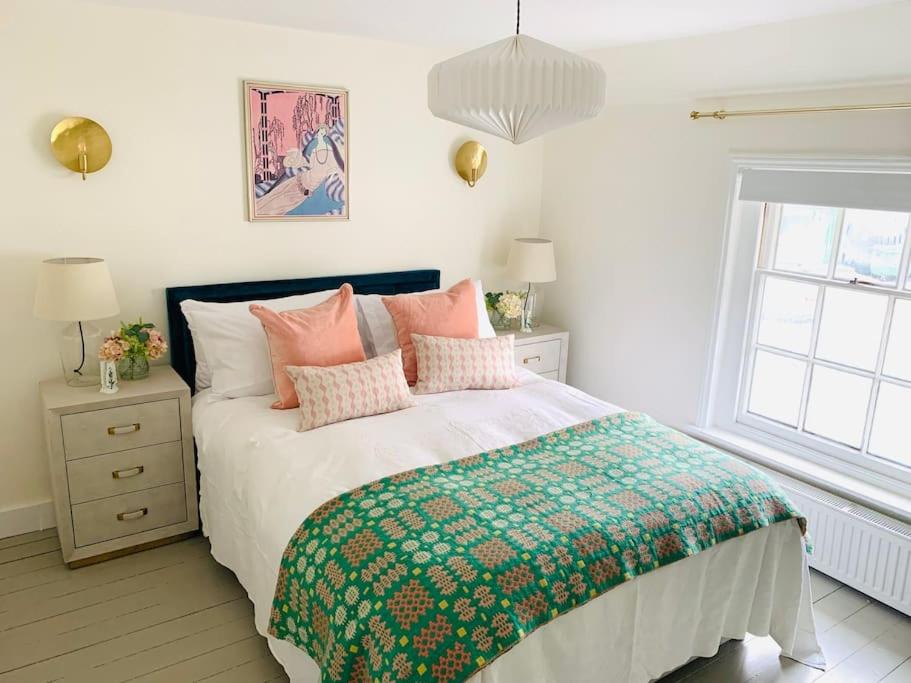 Un dormitorio con una cama con almohadas rosas y una ventana en The Yellow cottage on the hill., en Framlingham