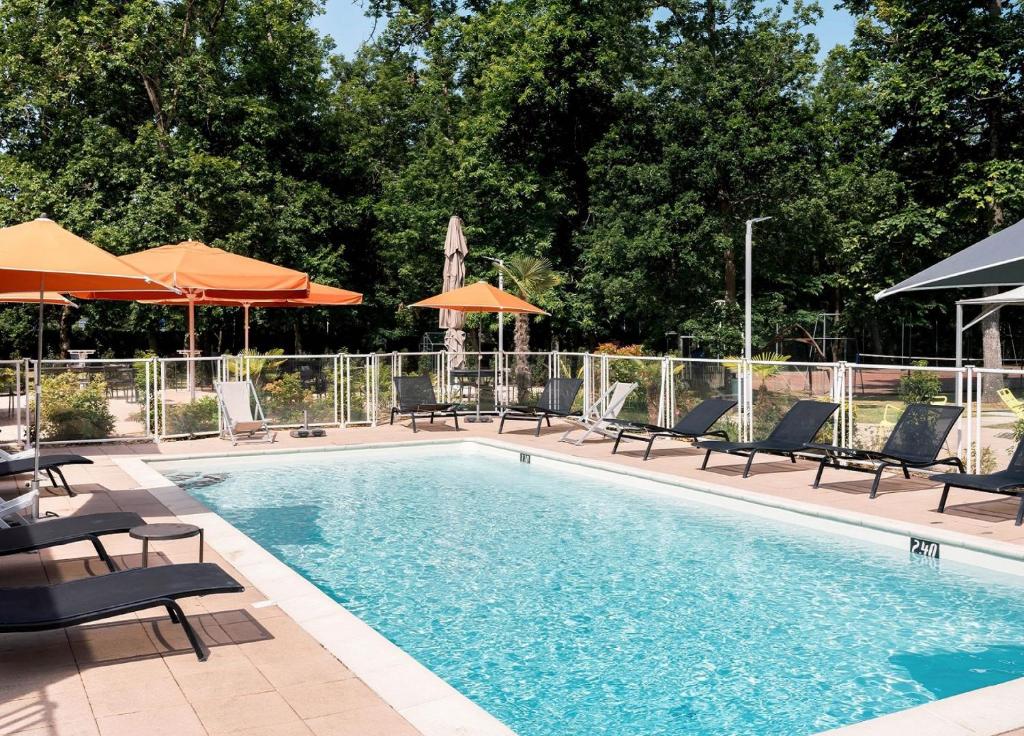 a swimming pool with lounge chairs and umbrellas at Novotel Orléans Sud La Source in Orléans