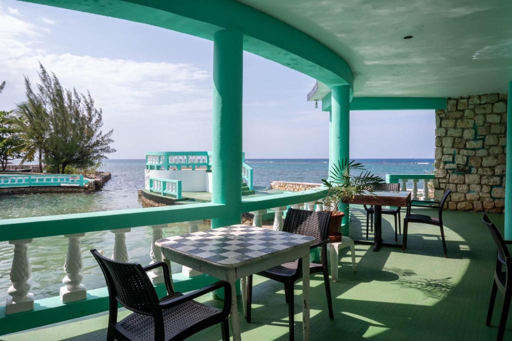 un porche con mesas y sillas y el océano en Ocean Front Triple Room at Sahara Hotel, en Montego Bay