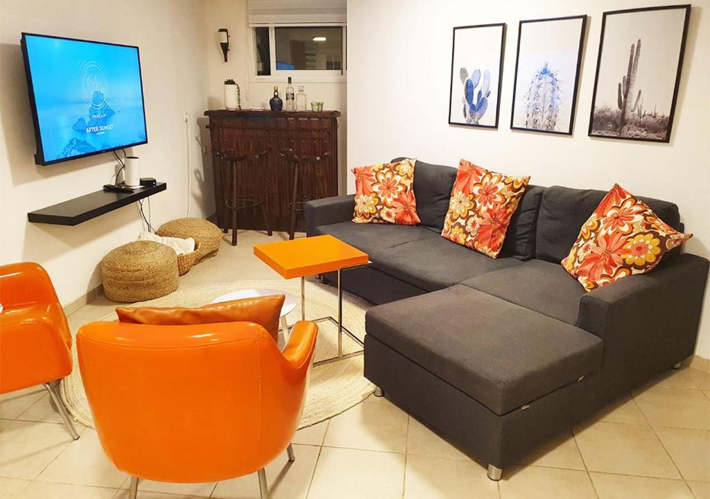 uma sala de estar com um sofá preto e cadeiras laranja em Spacious and Peaceful 2BD with a Garden & Parking em Gan H̱ayyim