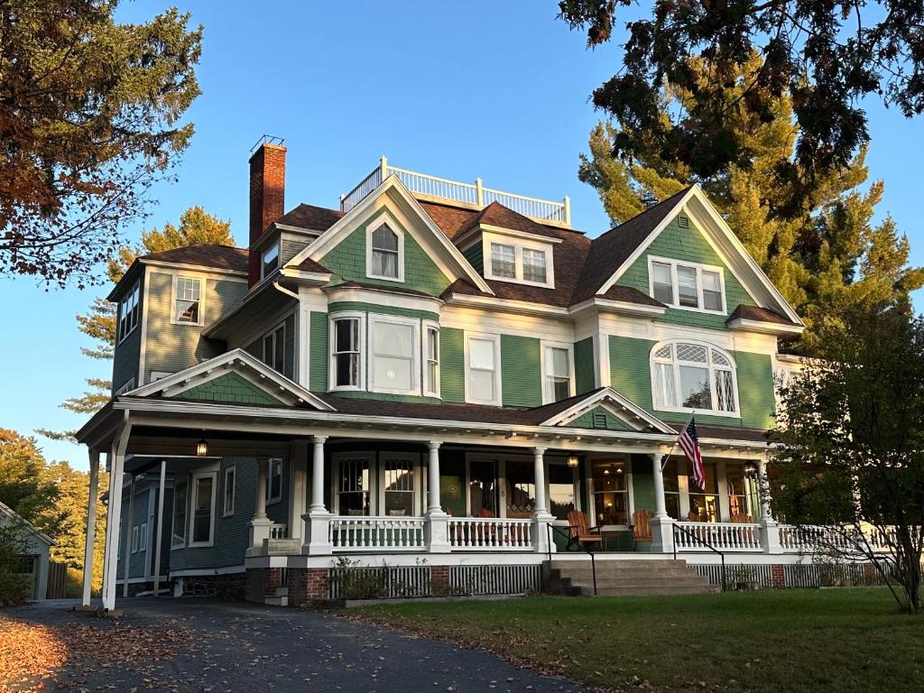 Franklin Manor Bed and Breakfast في سارانك ليك: منزل أخضر كبير مع شرفة على شارع