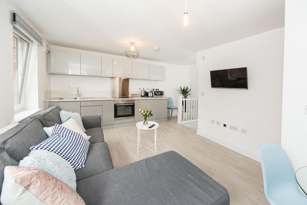 a living room with a gray couch and a kitchen at Wakefield City Centre 1 minute walk to station 2 bedroom townhouse with parking in Wakefield