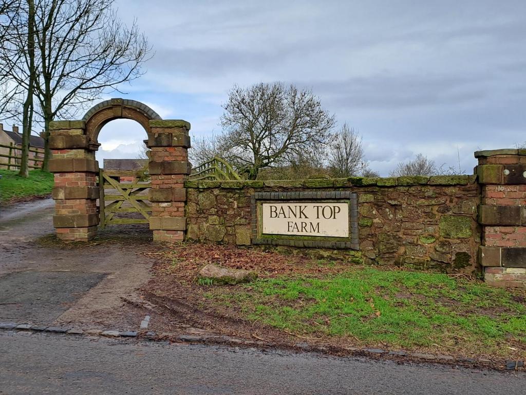 una recinzione di mattoni con un cartello che legge la fattoria in cima alla banca di Bank Top Farm Cottages a Stoke on Trent
