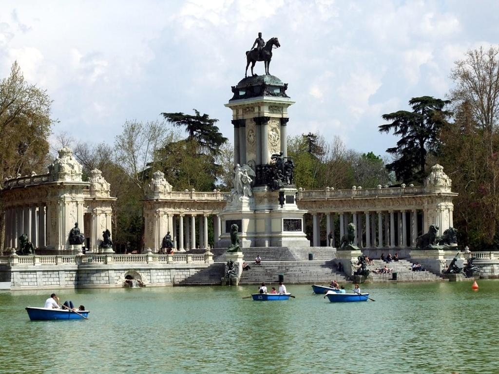 people in boats in the water in front of a building at La Casita del Retiro in Madrid