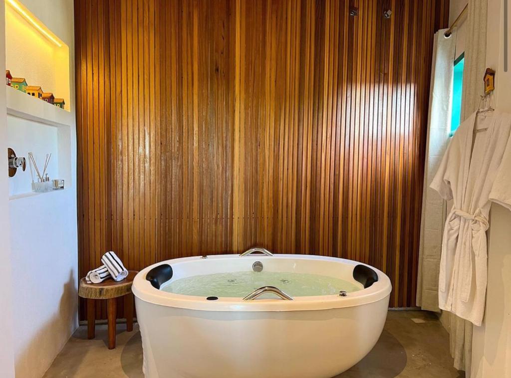 a bath tub in a bathroom with a wooden wall at Flô Casa Hotel in Trancoso