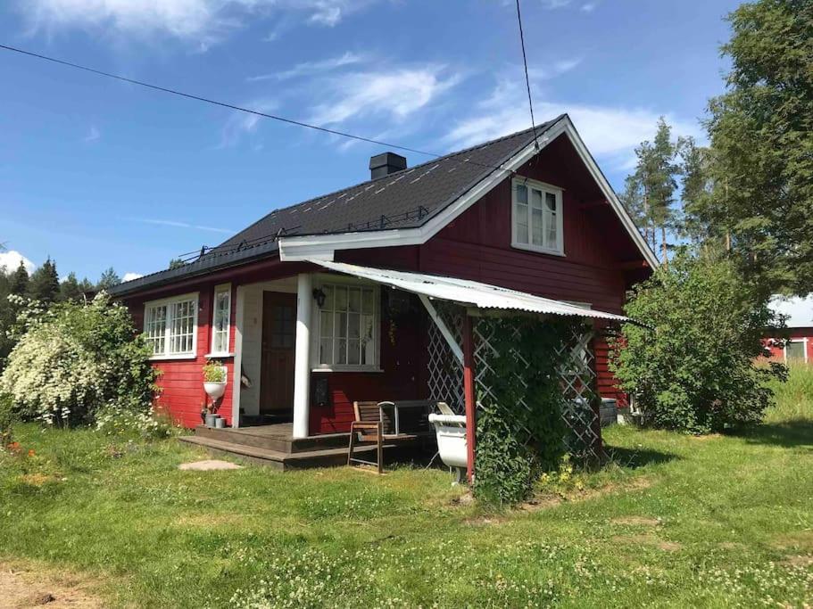 ein kleines rotes Haus mit einer Veranda auf einem Rasen in der Unterkunft Koselig hytte, nær Finnskogen og Vålerbanen in Åsnes