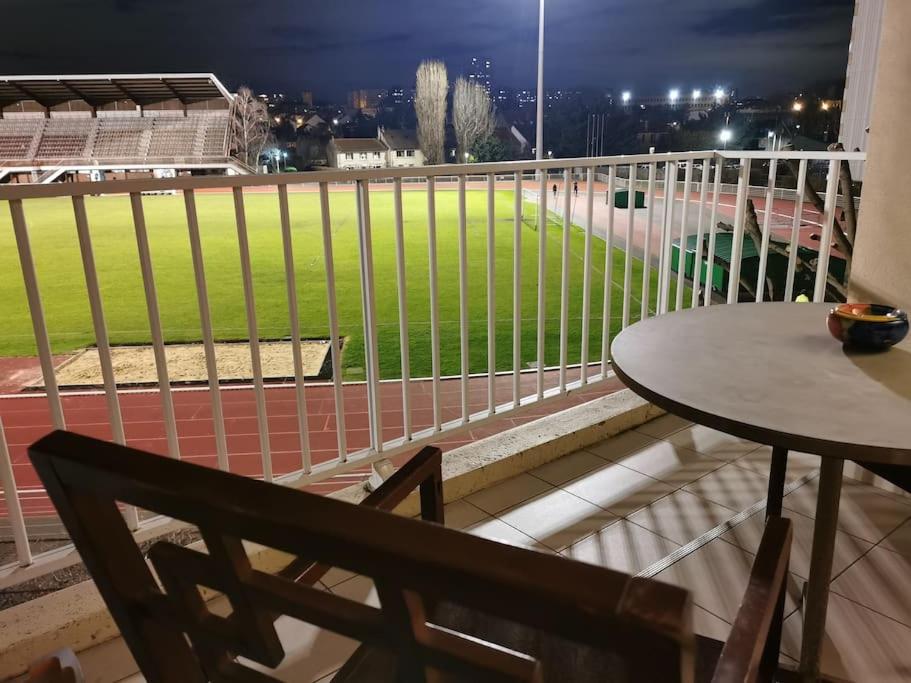 einen Balkon mit einem Tisch und Blick auf ein Baseballfeld in der Unterkunft Appartement entier in Cachan