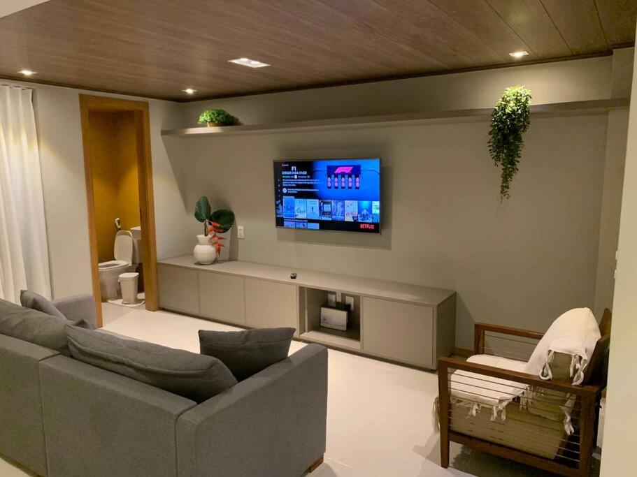 a living room with a couch and a tv on the wall at 4 Suítes Pé na Areia Itacimirim in Camacari