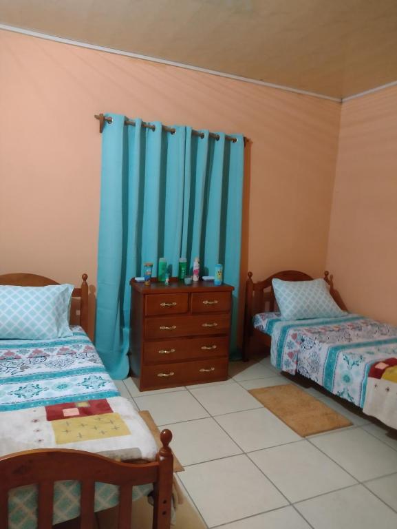 a bedroom with two beds and a dresser and blue curtains at Tessa's Inn in Arima