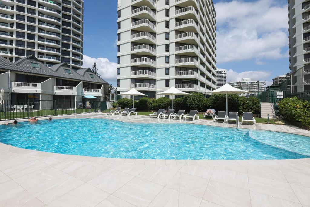 a swimming pool with chairs and umbrellas in front of buildings at The Breakers in Gold Coast