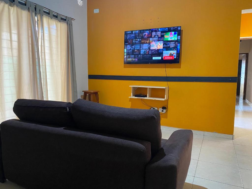 sala de estar con sofá y TV en una pared amarilla en Casa tranquila y cómoda, muy cerca del centro en Tunuyán