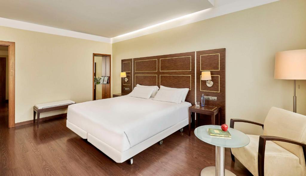 a bedroom with a white bed and a table and a chair at NH Gran Hotel Casino de Extremadura in Badajoz