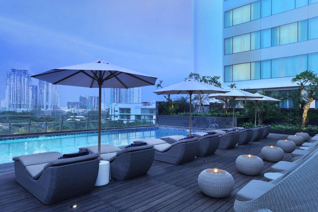 DoubleTree by Hilton Jakarta Kemayoran في جاكرتا: صف من الكراسي والمظلات بجانب المسبح