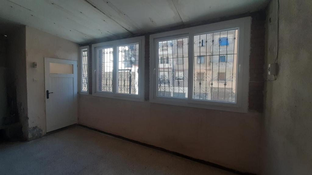 an empty room with three windows and a door at Chambres individuelles et collectives à Setif in Sétif