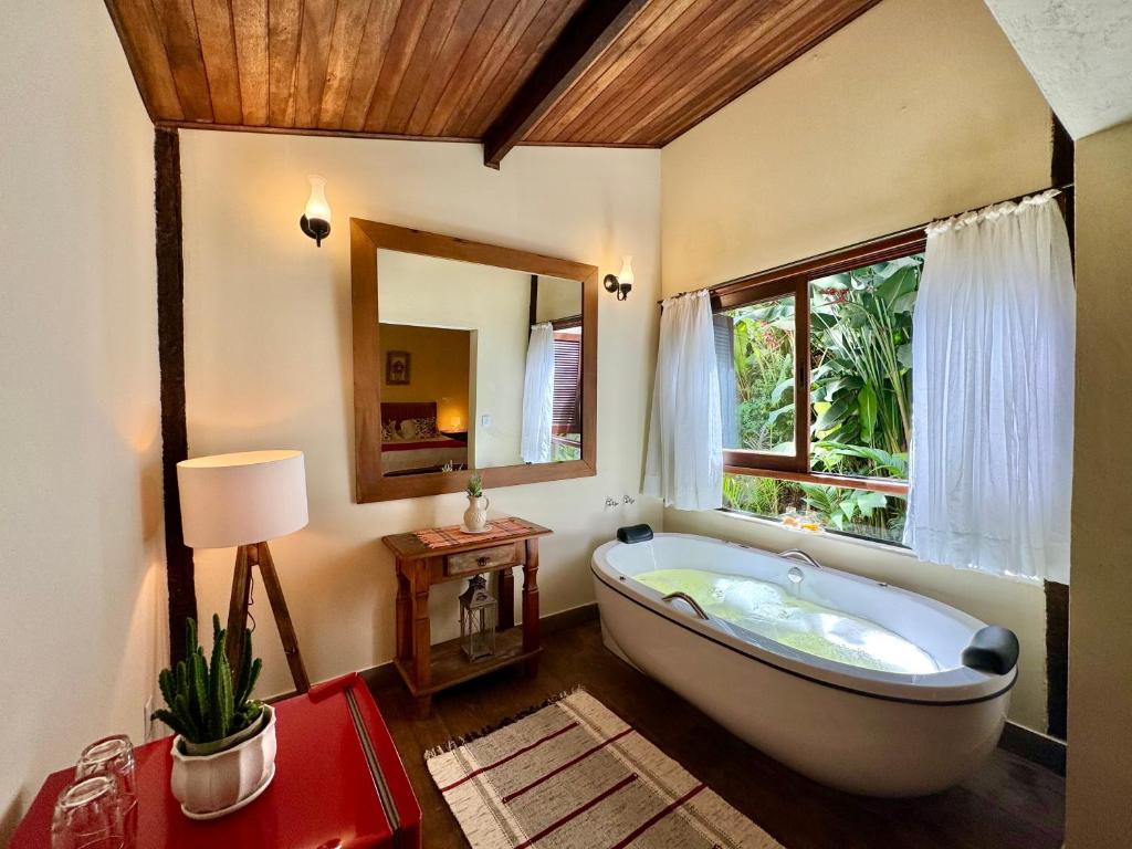 uma casa de banho com uma banheira grande e uma janela em Pousada Chalés Jardim das Bromélias - Visconde de Mauá em Viscode de Mauá