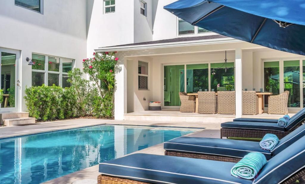 a house with a swimming pool with chairs and an umbrella at The Sapphire Villa - LUX 5 Bed in West Palm Beach