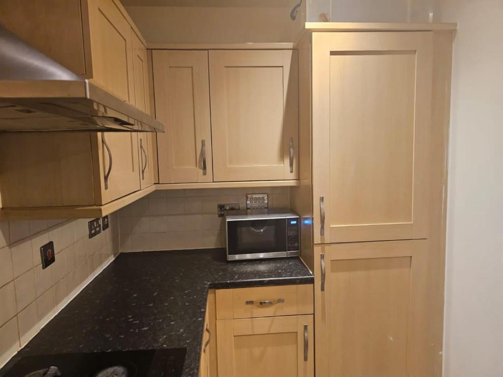 cocina con armarios de madera y microondas en Big double room with bathroom in 2 bedroom flat kitchen is shared, en Harrow on the Hill