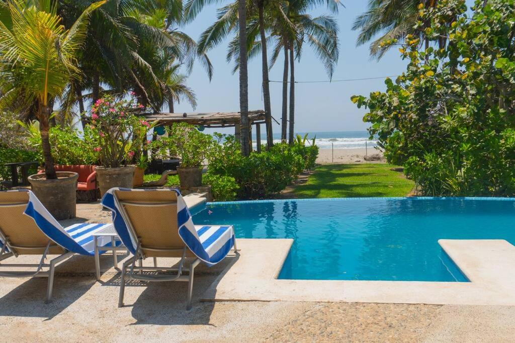 a swimming pool with two chairs and the beach at Casa de Playa Barra Vieja Acapulco in Barra Vieja