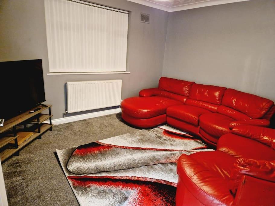 a living room with a red couch and a television at Malborough - a lovely 3 bed house for short or long-term stays in Derby