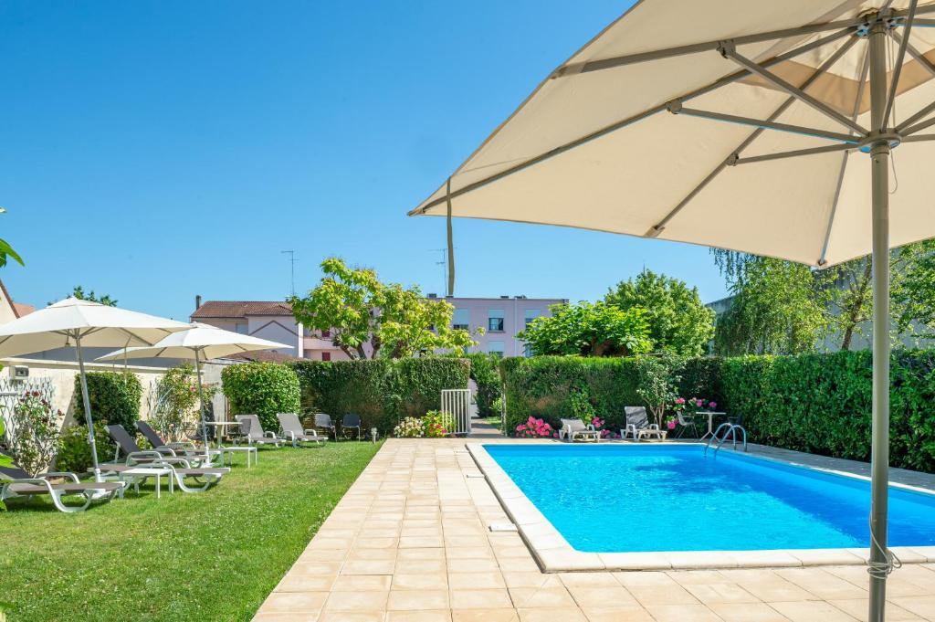 uma piscina com um guarda-sol ao lado de um quintal com cadeiras em Brit Hotel Europ Bergerac em Bergerac