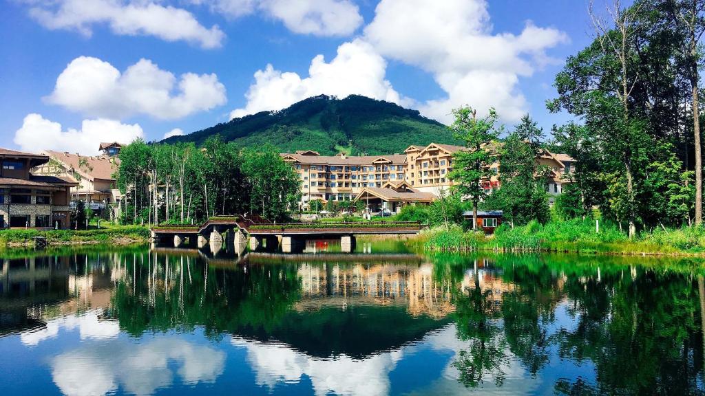 a reflection of a building in a lake with a mountain at Wanda Jin Suites Changbaishan in Fusong