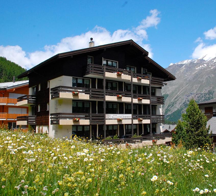 a building on a hill with a field of flowers at Hotel Garni Jägerhof in Saas-Fee
