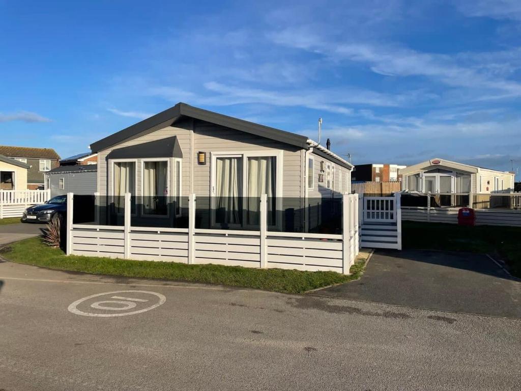 a house with a white fence next to a street at 42 Woodland Walk Pevensey Bay Holiday Park sleeps 6 in Pevensey