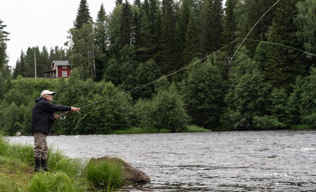 un hombre de pie en un río sosteniendo una línea de pesca en Cabin by Byske river surrounded by the forest en Byske