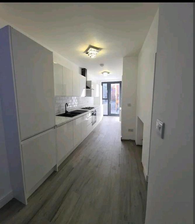 an empty kitchen with white cabinets and a wooden floor at Impeccable 2-Bed Apartment in London in Hendon