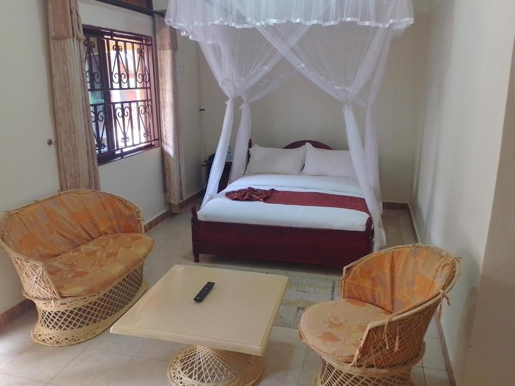 Mbarara的住宿－Acacia Country Inn，一间卧室配有一张床、两把椅子和一张桌子