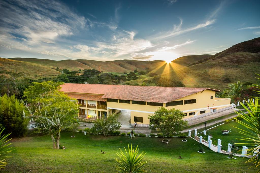 a building with the sun setting in the mountains at Pousada Luar do Sertão in Valença