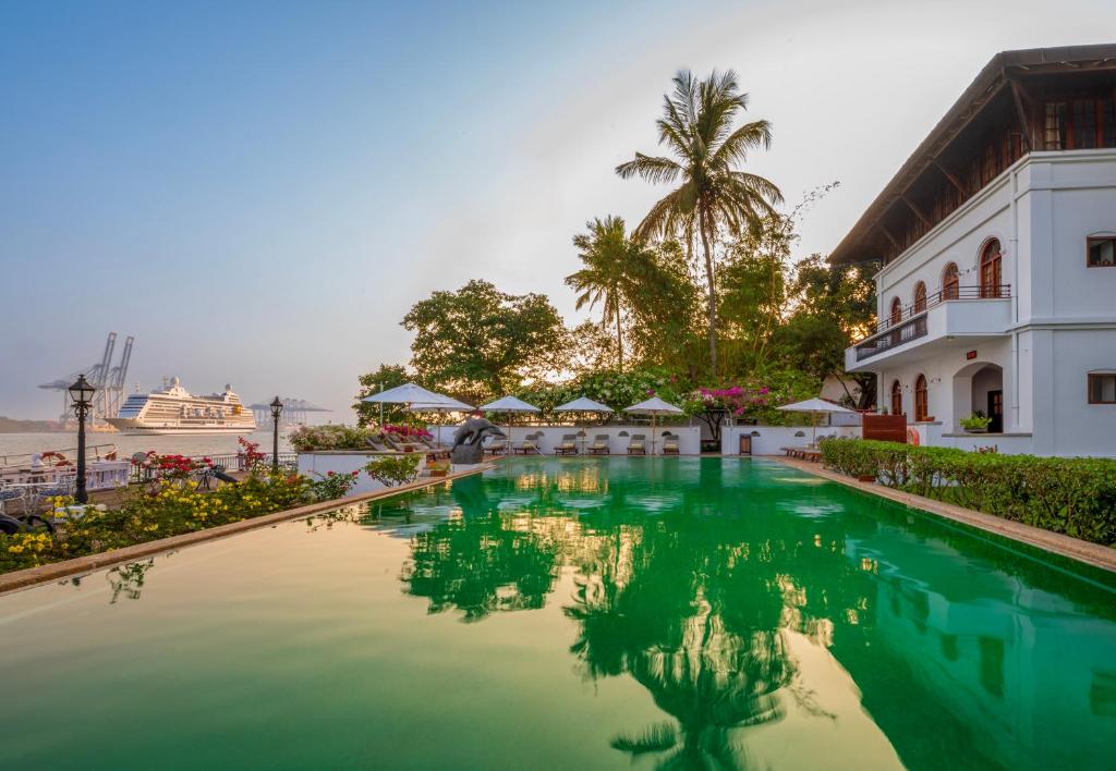 a swimming pool in front of a building with a palm tree at Brunton Boatyard - CGH Earth in Cochin