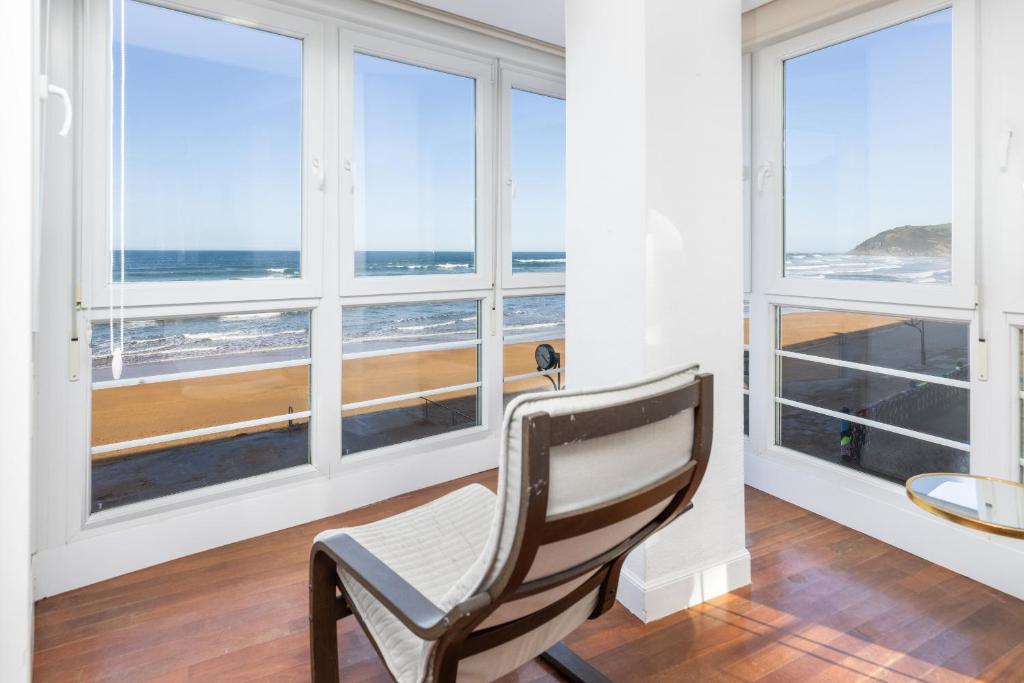 uma cadeira num quarto com janelas com vista para o oceano em Primera línea de playa con parking - Zarautz em Zarautz