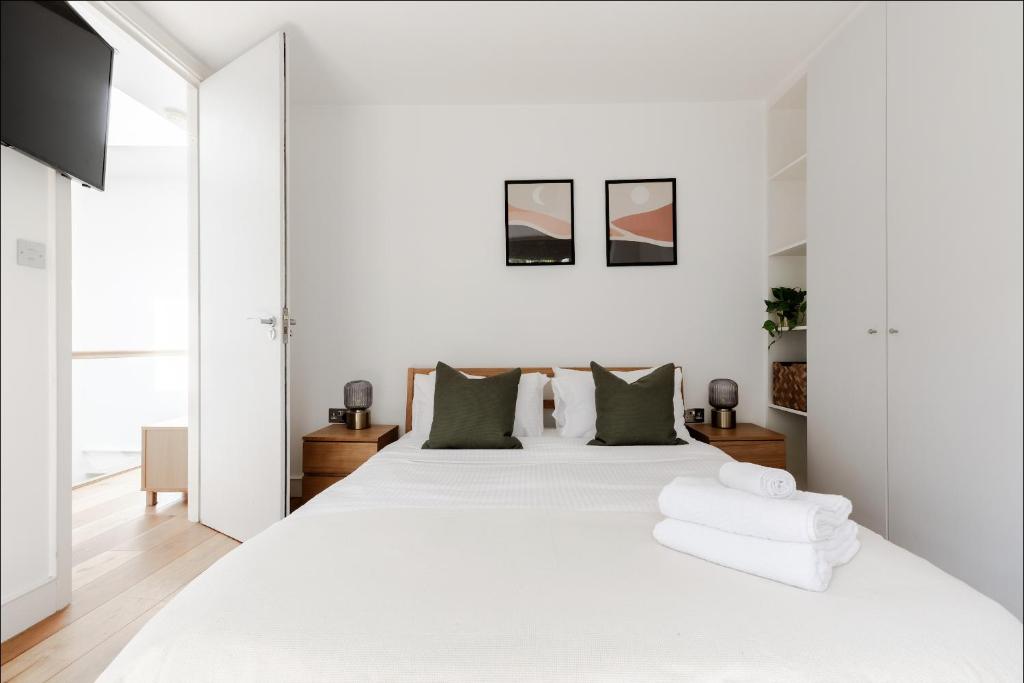 a white bedroom with a large white bed with green pillows at Spacious and sunlit 3-bedroom apartment near Paddington Station in London