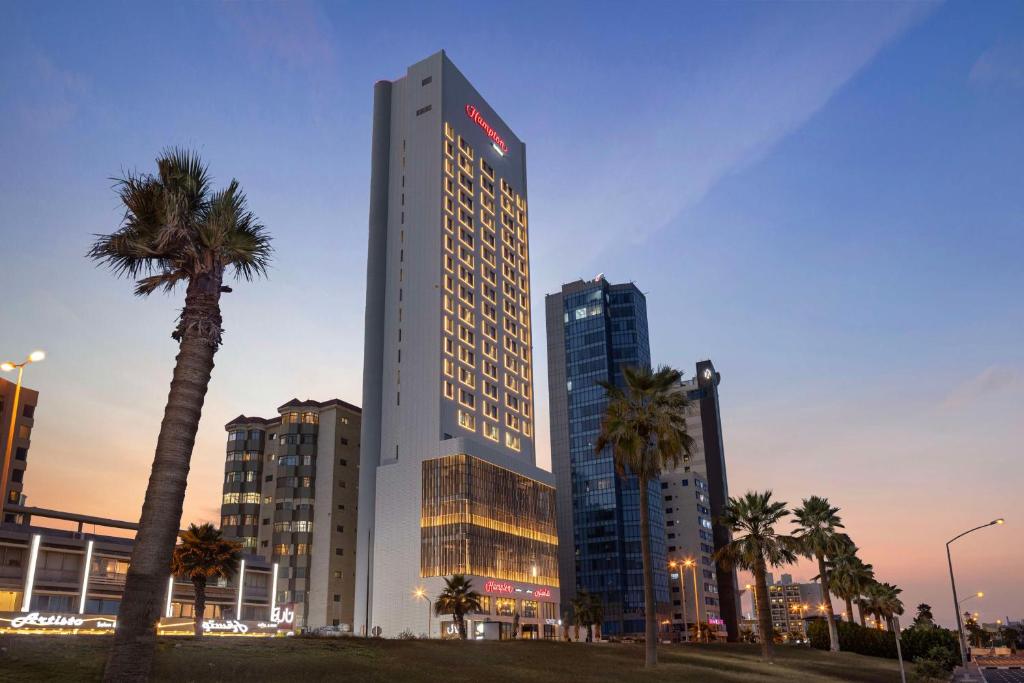 a tall building with palm trees in front of it at Hampton By Hilton Kuwait Salmiya in Kuwait