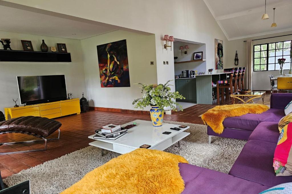 sala de estar con sofás morados y TV en Pumbaa Farmhouse + Cottages, en Nairobi